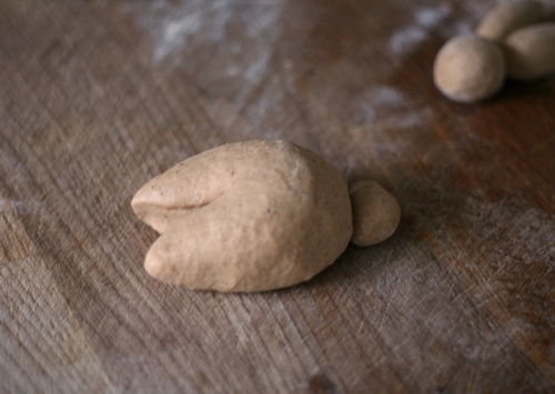 Using a little dab of water, attach the tail. Shape the two front paws by cutting approx. 1/3 of the length of the dough, dividing the front part into 2, just like with the ears.