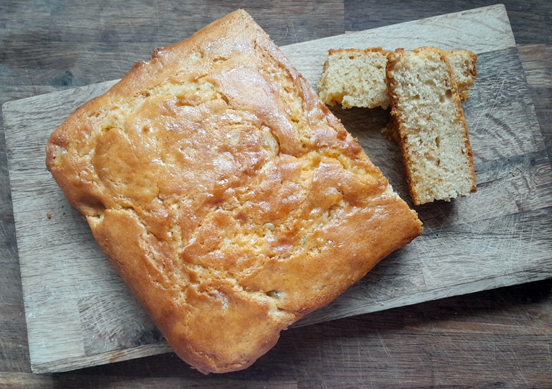 A square lime marmalade cake with two pieces cut off and displayed, on a wooden cutting board.