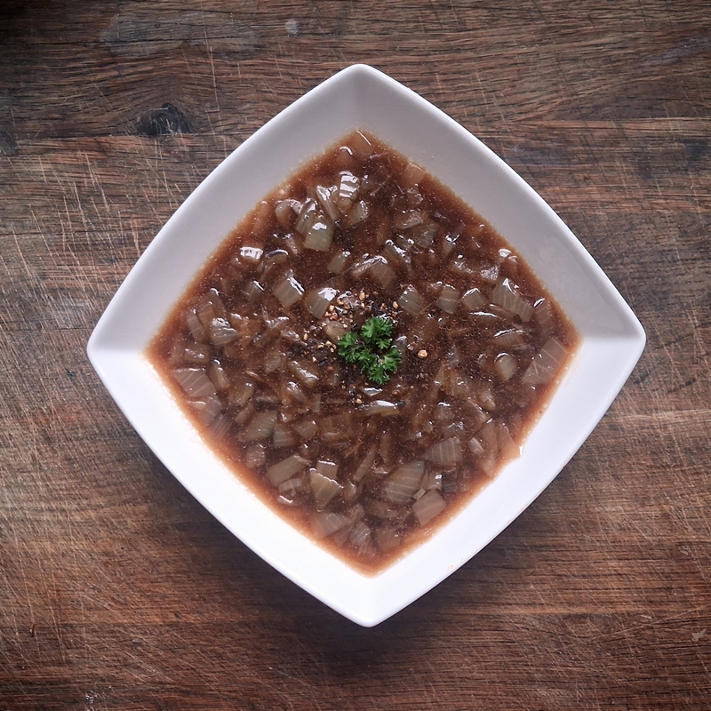 A bowl of onion soup, showing chopped onion in a dark meat broth